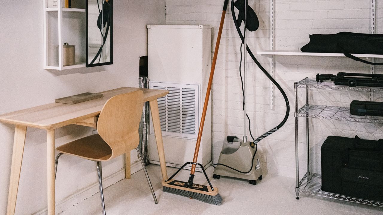 our-story A tidy home office space featuring a wooden desk, chair, broom, and cleaning equipment.
